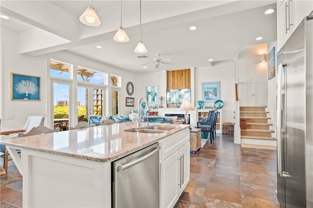 kitchen with white cabinets, sink, an island with sink, light stone countertops, and appliances with stainless steel finishes