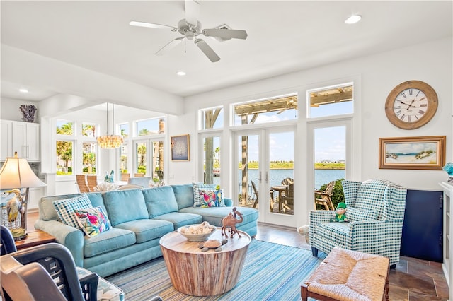 sunroom / solarium with ceiling fan with notable chandelier, a water view, and french doors