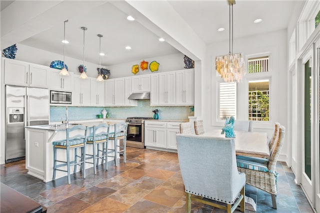 kitchen with built in appliances, white cabinetry, a kitchen breakfast bar, decorative light fixtures, and decorative backsplash