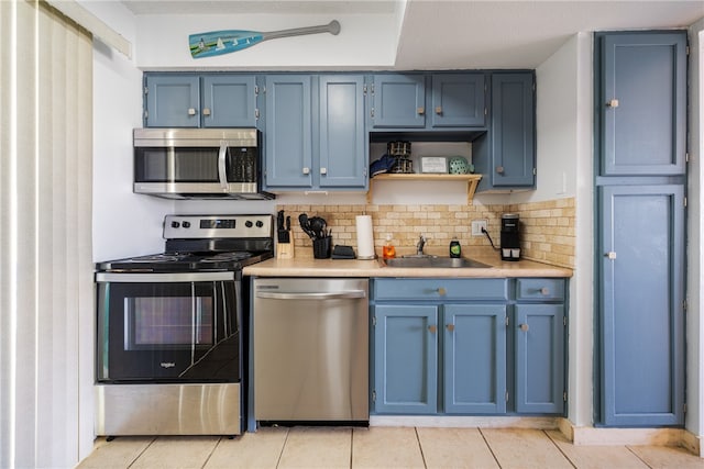 kitchen with blue cabinetry, light tile patterned floors, stainless steel appliances, and sink