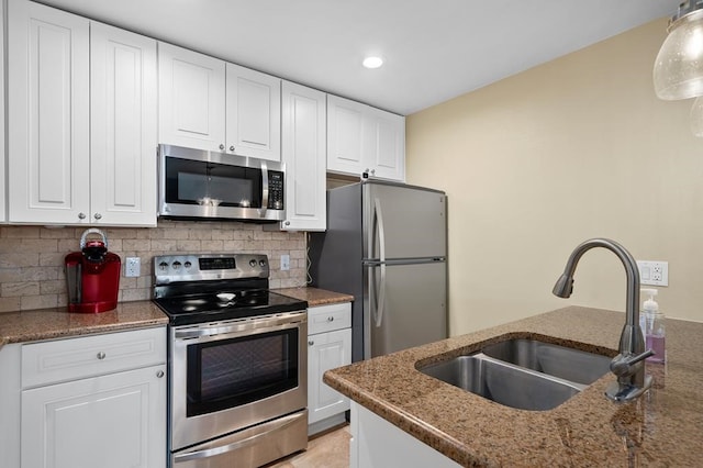 kitchen with stainless steel appliances, white cabinetry, hanging light fixtures, sink, and dark stone countertops