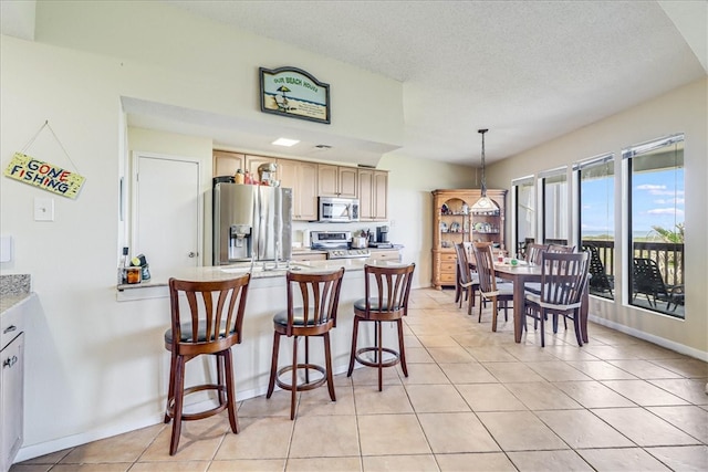 kitchen with stainless steel appliances, light tile patterned flooring, light brown cabinetry, a textured ceiling, and pendant lighting