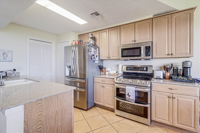 kitchen with light brown cabinetry, sink, light tile patterned flooring, and stainless steel appliances