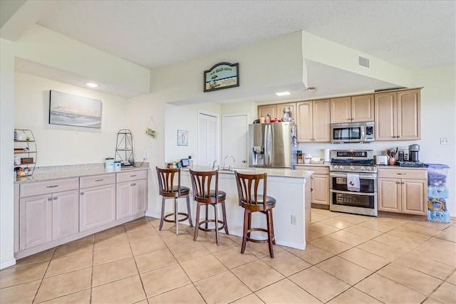 kitchen with a textured ceiling, stainless steel appliances, light tile patterned flooring, and light brown cabinetry