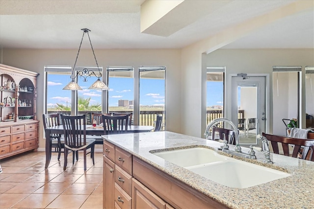 kitchen with light tile patterned floors, sink, pendant lighting, and light stone counters