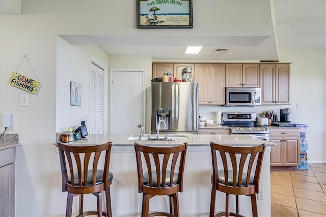 kitchen featuring light brown cabinetry, appliances with stainless steel finishes, light tile patterned floors, and a kitchen breakfast bar