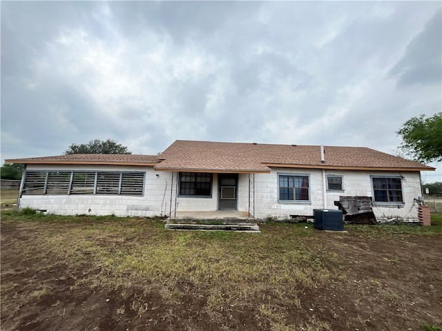 rear view of property with central AC unit and a lawn