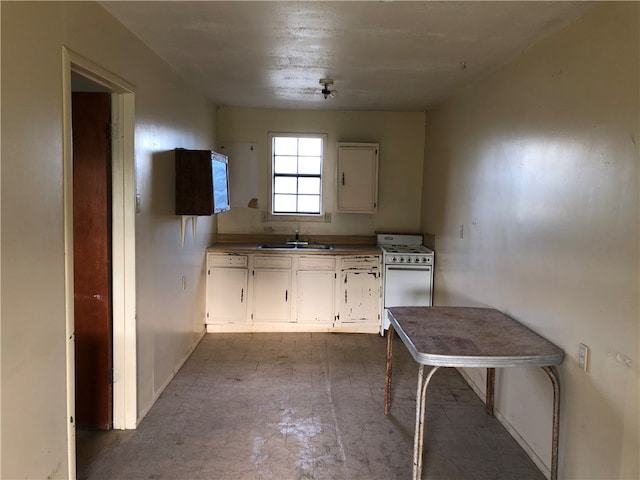 kitchen with white stove, sink, and white cabinets