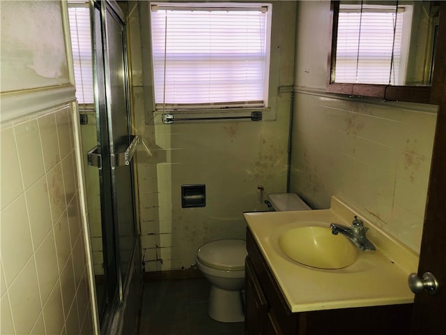 bathroom featuring a wealth of natural light, a shower with door, vanity, and tile walls