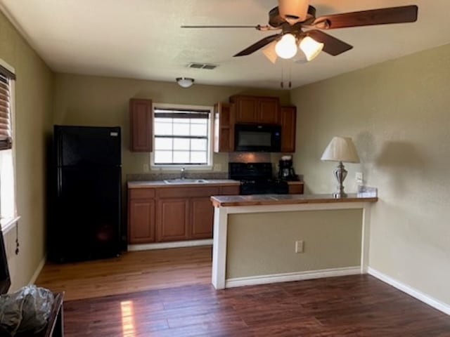 kitchen with dark wood-type flooring, kitchen peninsula, black appliances, sink, and ceiling fan