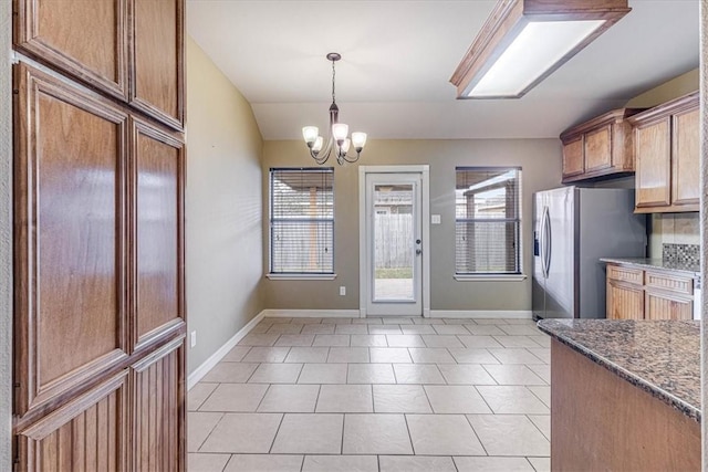 kitchen with an inviting chandelier, hanging light fixtures, stainless steel fridge, and a healthy amount of sunlight