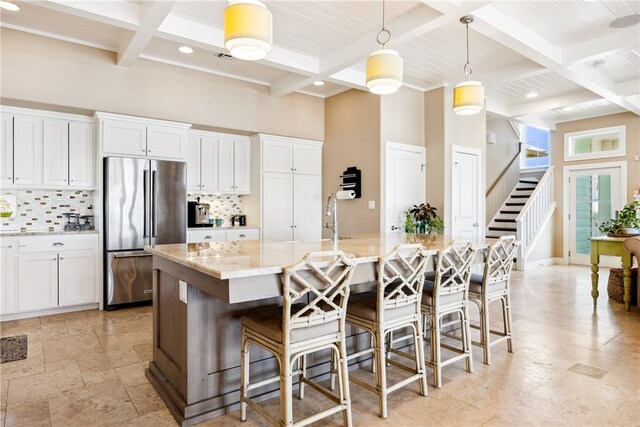 kitchen featuring decorative light fixtures, an island with sink, white cabinets, beamed ceiling, and high end fridge