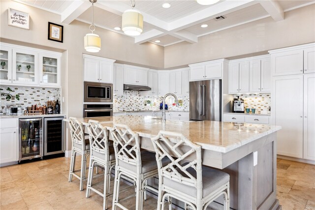 kitchen featuring appliances with stainless steel finishes, decorative light fixtures, light stone countertops, beverage cooler, and a kitchen island with sink