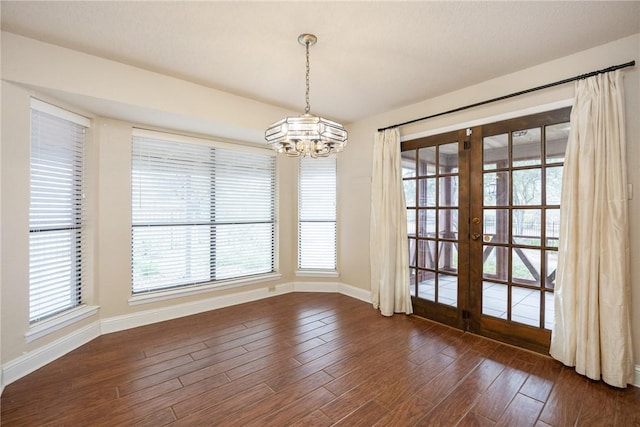 unfurnished dining area featuring french doors, dark wood-type flooring, and an inviting chandelier