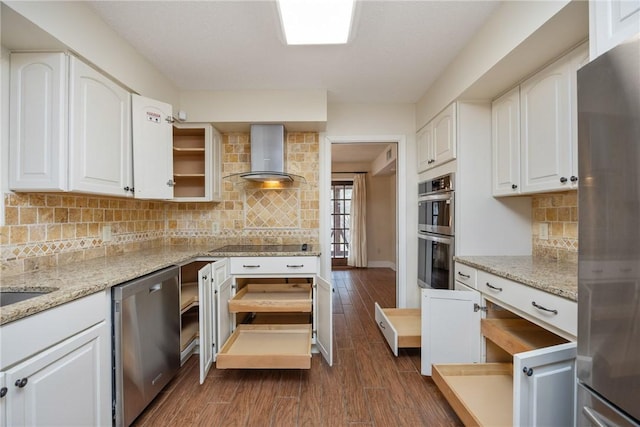 kitchen featuring white cabinets, stainless steel appliances, light stone counters, and wall chimney exhaust hood