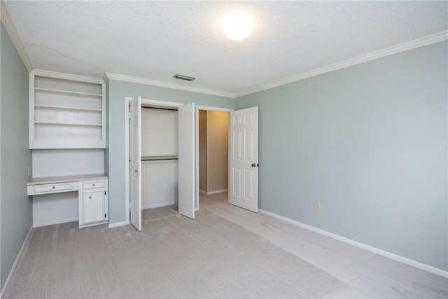 unfurnished bedroom with light carpet, crown molding, built in desk, a textured ceiling, and a closet