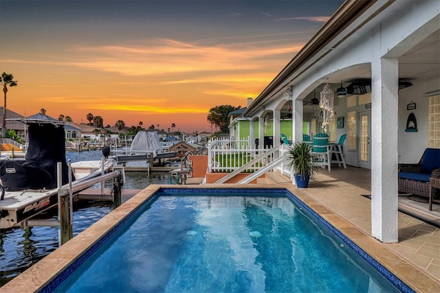 pool at dusk with a water view, a boat dock, and a patio