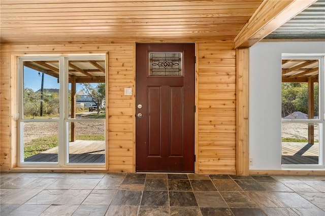 doorway to outside with wood ceiling, plenty of natural light, and wooden walls