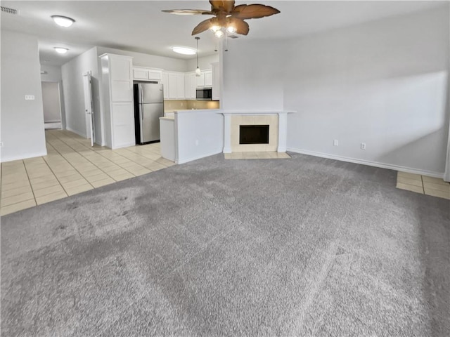 unfurnished living room featuring ceiling fan, light tile patterned floors, a tile fireplace, light carpet, and baseboards