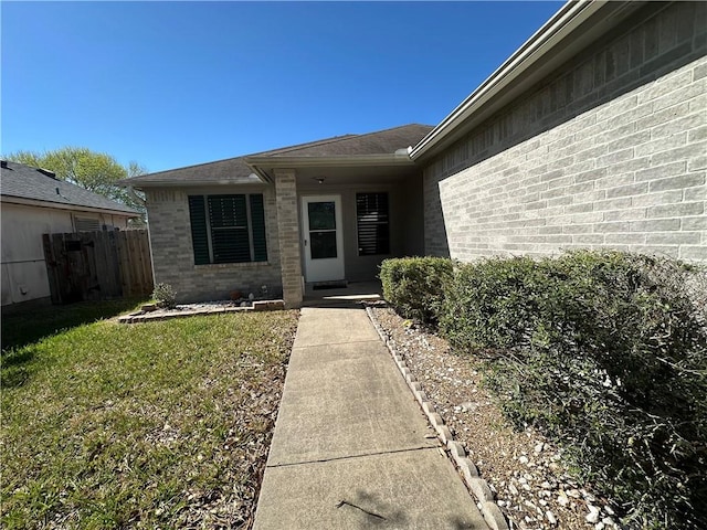 view of exterior entry with brick siding, a yard, and fence