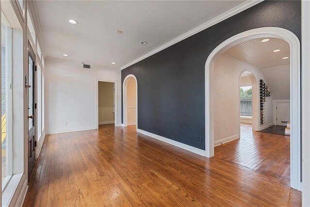 empty room with arched walkways, ornamental molding, wood finished floors, recessed lighting, and baseboards