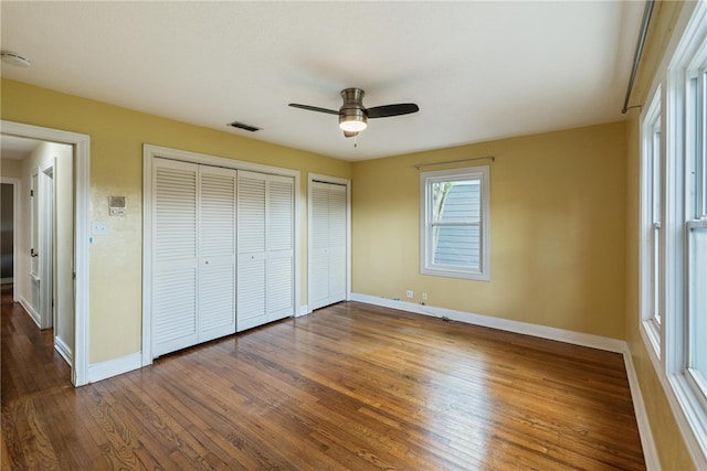 unfurnished bedroom with wood-type flooring, ceiling fan, and two closets