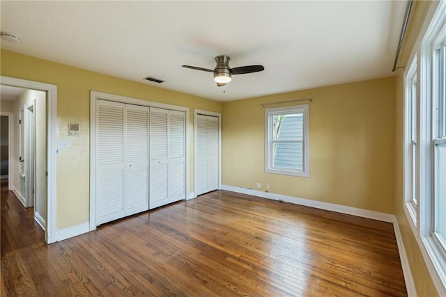 unfurnished bedroom featuring multiple closets, baseboards, wood finished floors, and a ceiling fan