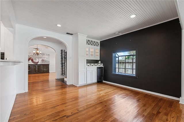 unfurnished living room featuring arched walkways, a chandelier, light wood-style flooring, crown molding, and recessed lighting