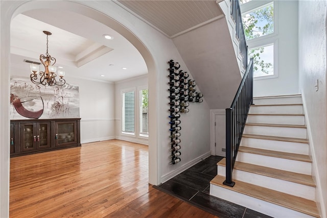 staircase featuring a tray ceiling, wood-type flooring, a chandelier, and ornamental molding