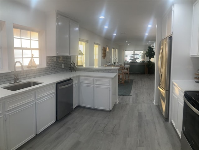 kitchen with appliances with stainless steel finishes, a sink, a peninsula, light countertops, and white cabinets