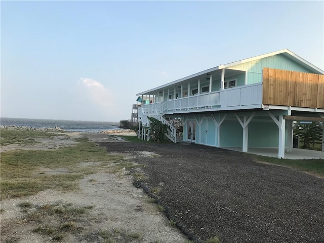 view of front facade featuring stairs, dirt driveway, and a deck with water view