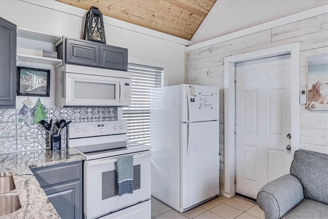 kitchen with wood walls, white appliances, light stone countertops, gray cabinetry, and light tile patterned floors