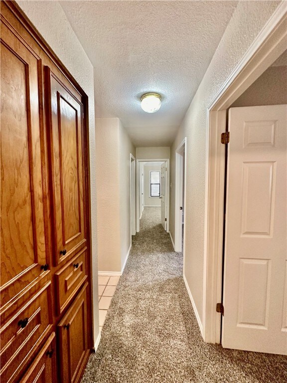 hall with a textured ceiling and light carpet