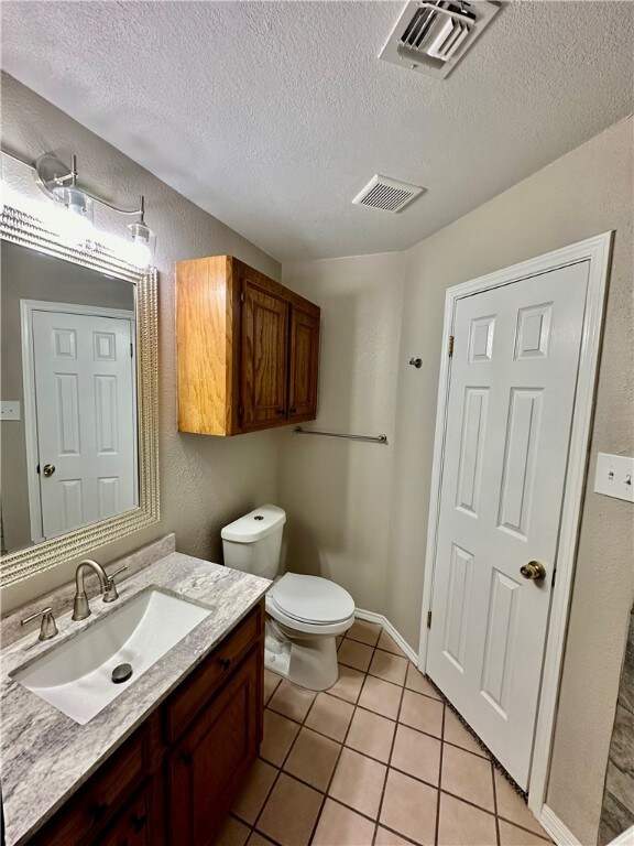 bathroom featuring vanity, tile patterned flooring, a textured ceiling, and toilet