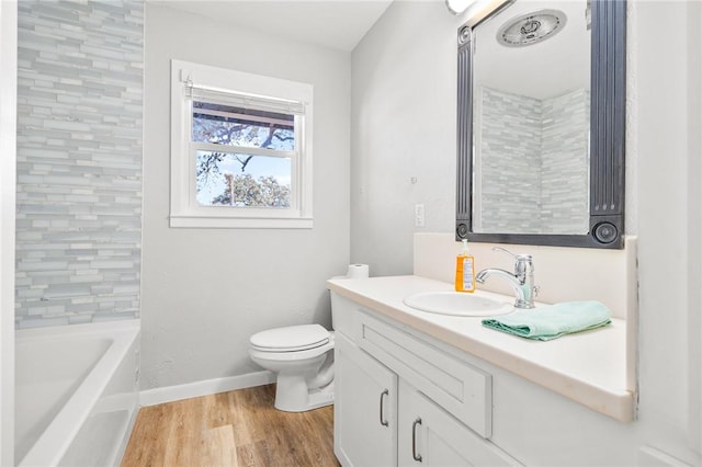 full bathroom with toilet, wood finished floors, baseboards, a bathtub, and vanity