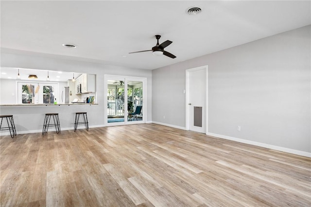 unfurnished living room with light wood-style flooring, a ceiling fan, visible vents, and baseboards