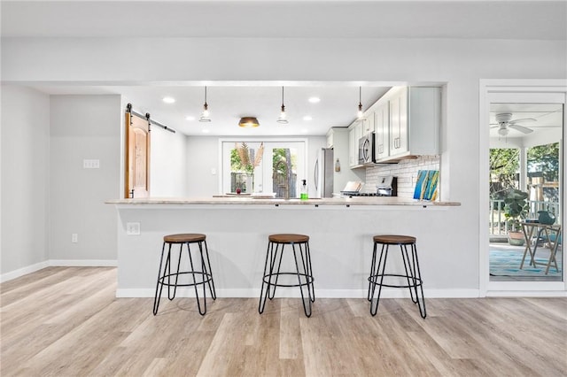 kitchen with light wood-style flooring, tasteful backsplash, a barn door, appliances with stainless steel finishes, and a breakfast bar area