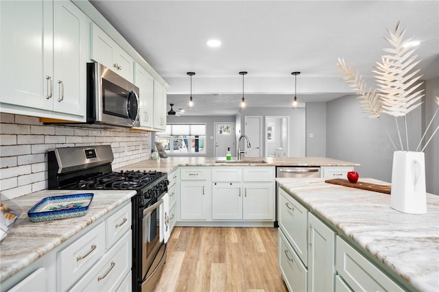 kitchen with a peninsula, a sink, stainless steel appliances, white cabinetry, and light wood-type flooring