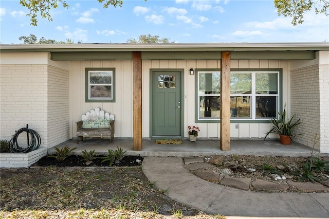 entrance to property featuring a porch, brick siding, and board and batten siding