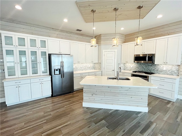 kitchen featuring white cabinetry, sink, appliances with stainless steel finishes, hanging light fixtures, and wooden walls