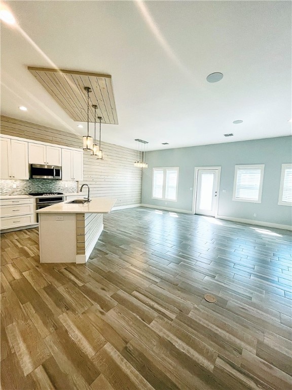 kitchen with stainless steel appliances, sink, wood-type flooring, white cabinets, and pendant lighting