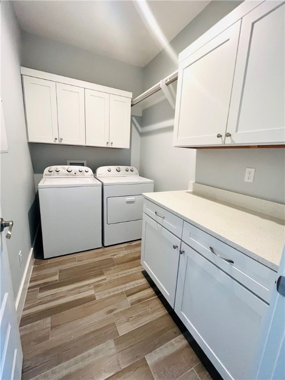 laundry room with washing machine and clothes dryer, cabinets, and light hardwood / wood-style flooring