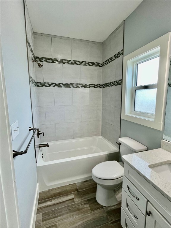 full bathroom featuring hardwood / wood-style flooring, vanity, toilet, and tiled shower / bath combo