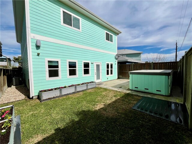 back of house with a hot tub, a patio, and a lawn