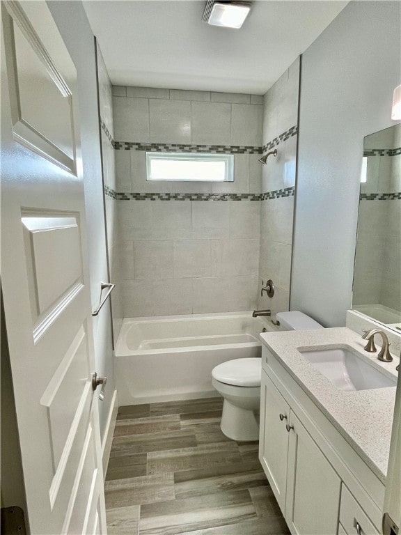 full bathroom with vanity, hardwood / wood-style flooring, tiled shower / bath, and toilet