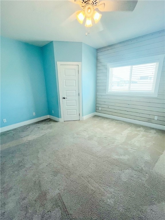 carpeted spare room with wooden walls and ceiling fan