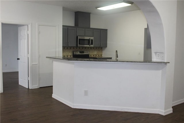 kitchen with appliances with stainless steel finishes, kitchen peninsula, decorative backsplash, and dark stone counters