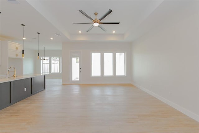 unfurnished living room featuring sink, a raised ceiling, ceiling fan, and light wood-type flooring