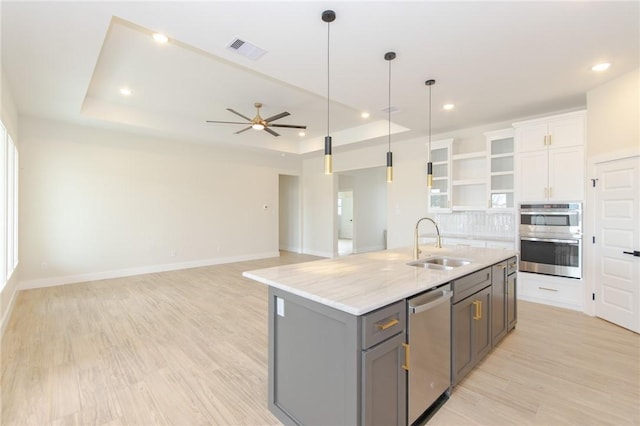 kitchen with sink, appliances with stainless steel finishes, a tray ceiling, white cabinets, and a center island with sink