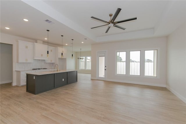 kitchen with pendant lighting, sink, a tray ceiling, white cabinets, and a large island with sink